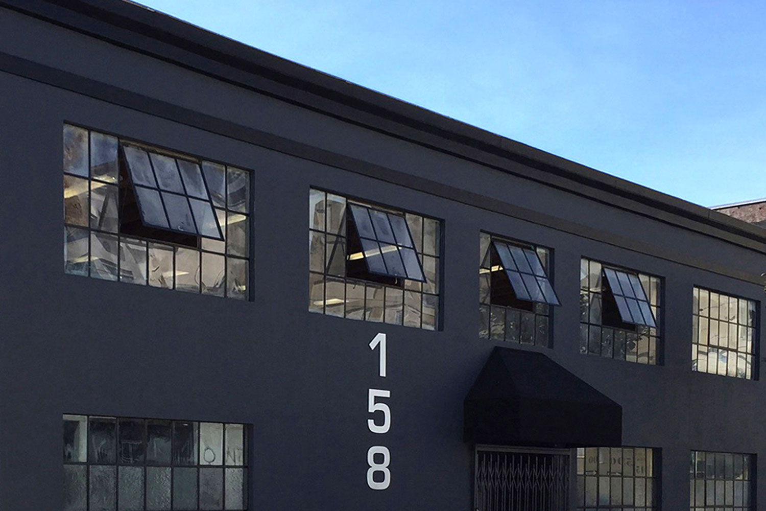 Two-story commercial real estate office building. Single tenant occupancy. Exterior painted dark gray with black trim. Walk-up entryway with canopy. Oversized windows.