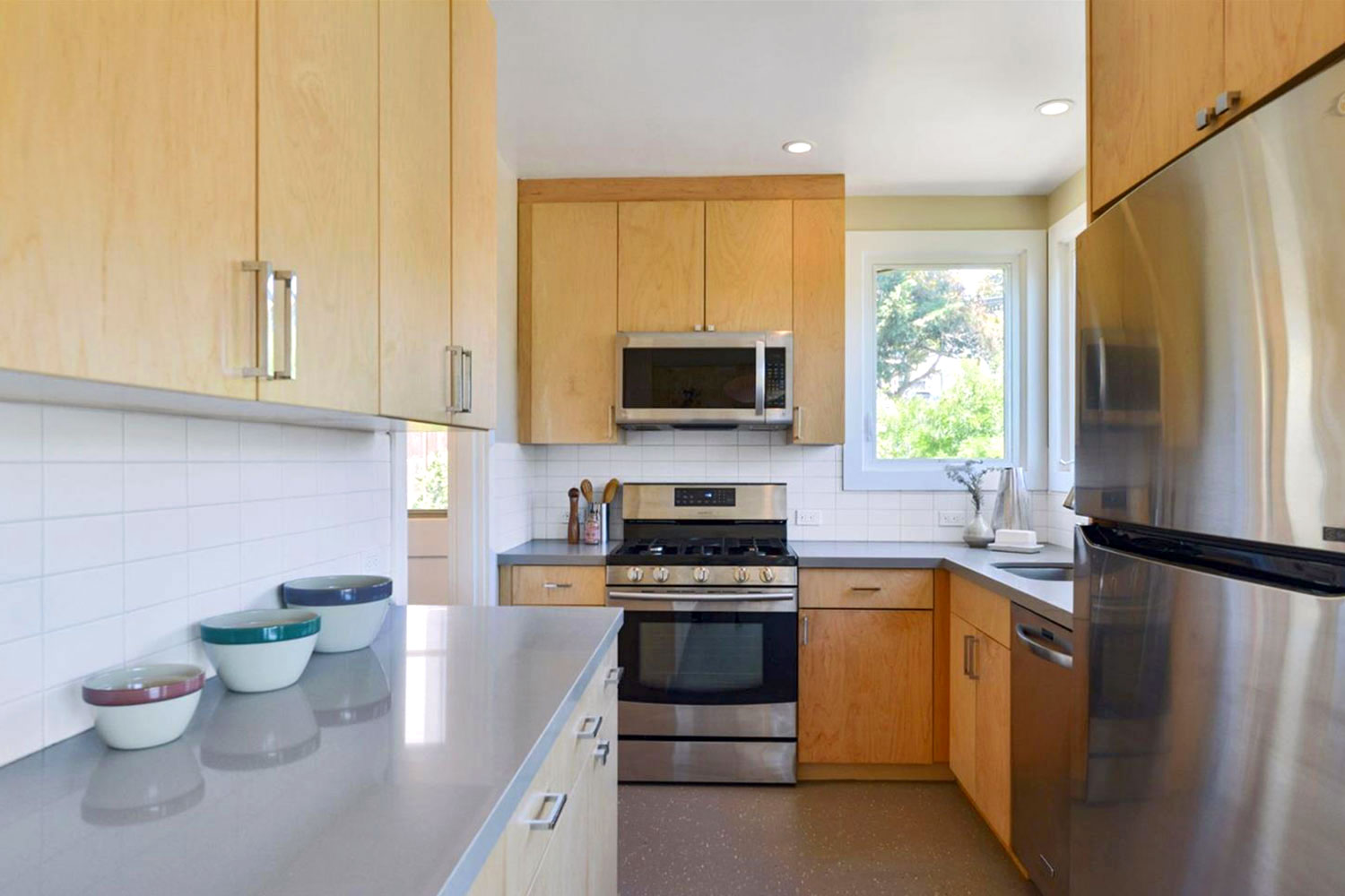 Renovated kitchen in a single family home. Light gray stone countertops, modern flat panel cabinets, white subway tile backsplash, and stainless steel appliances.