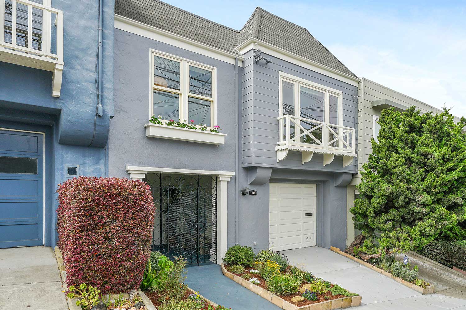 Mid-century, 2-story single family home. Exterior painted gray with white trim. Landscaped entry.