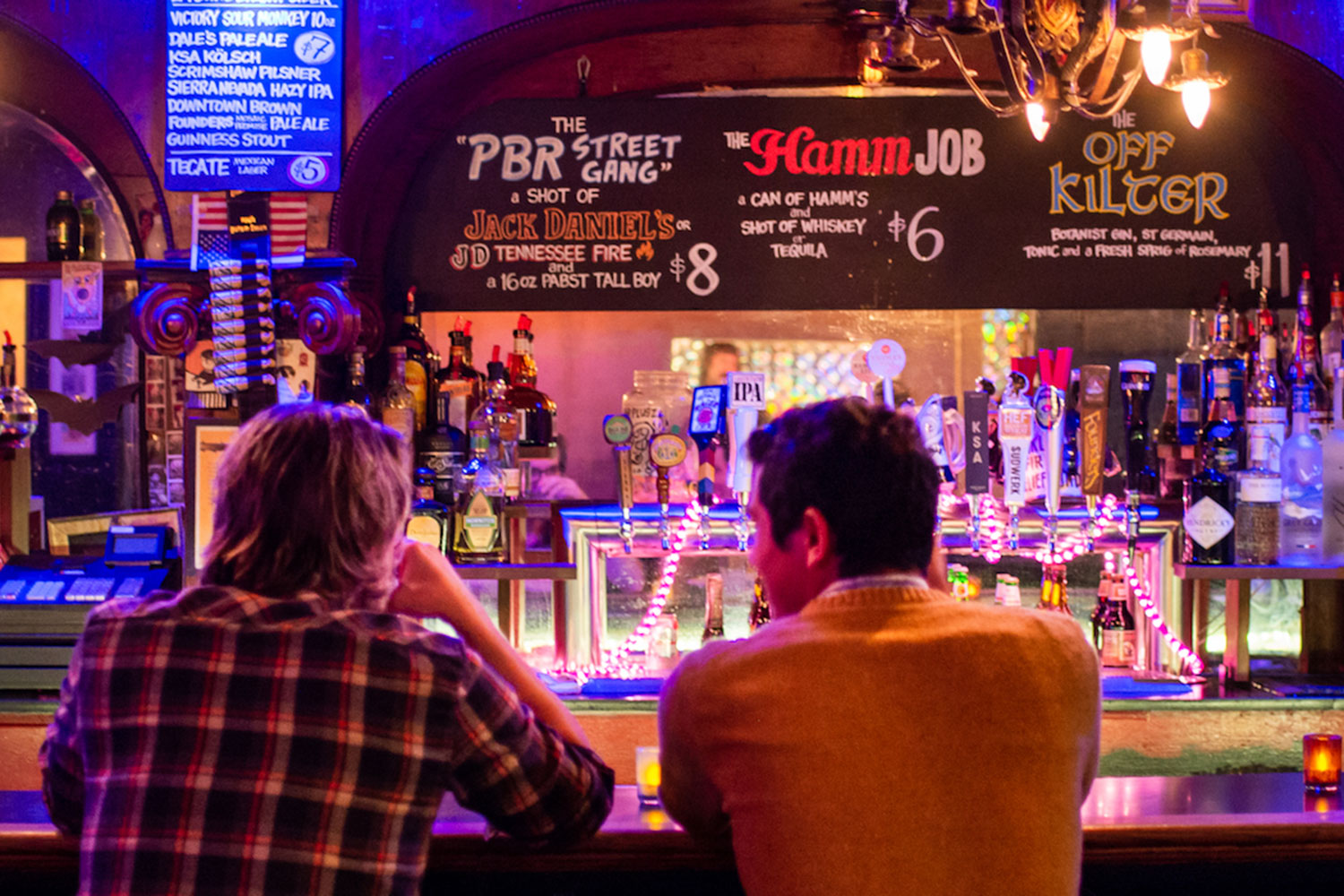 Bar interior. Beer taps, countertop, bar stools. Unique signage with drink names and pricing. Vintage lighting.