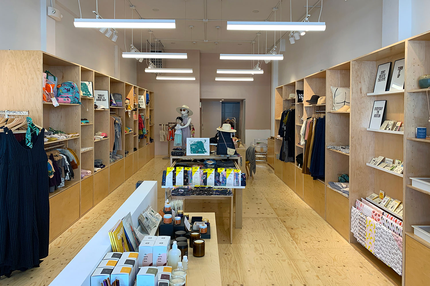 Interior shop. Custom built wood display racks with merchandise. Unique track lighting. Beige painted walls. Light colored hardwood floor.