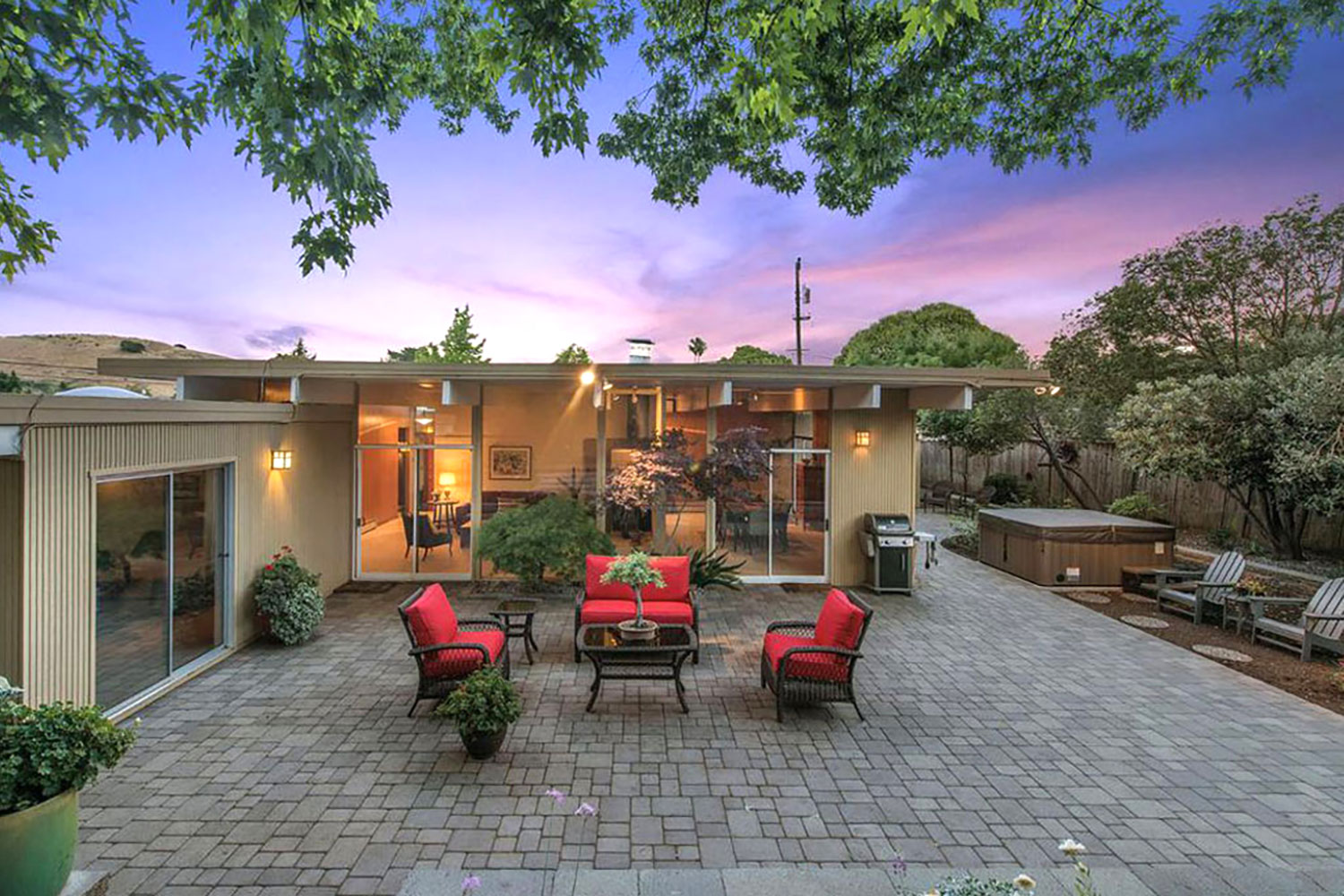 Mid-century Eichler designed home. Pitched roof with dramatic exposed beams, floor-to-ceiling windows. Exterior painted beige with brown trim. Landscaped patio with hot tub.