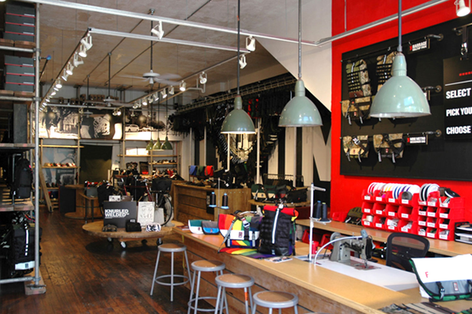 Retail shop interior. Custom display racks, unique canister style light fixtures, countertop work area with stools. Hardwood floors.